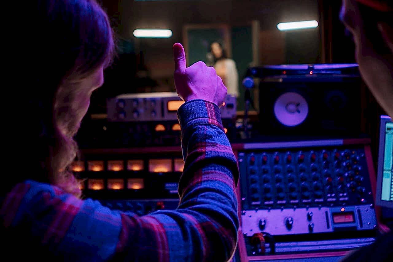hero-img-02 Audio engineer gesturing thumbs up in a vibrant music studio with equipment.