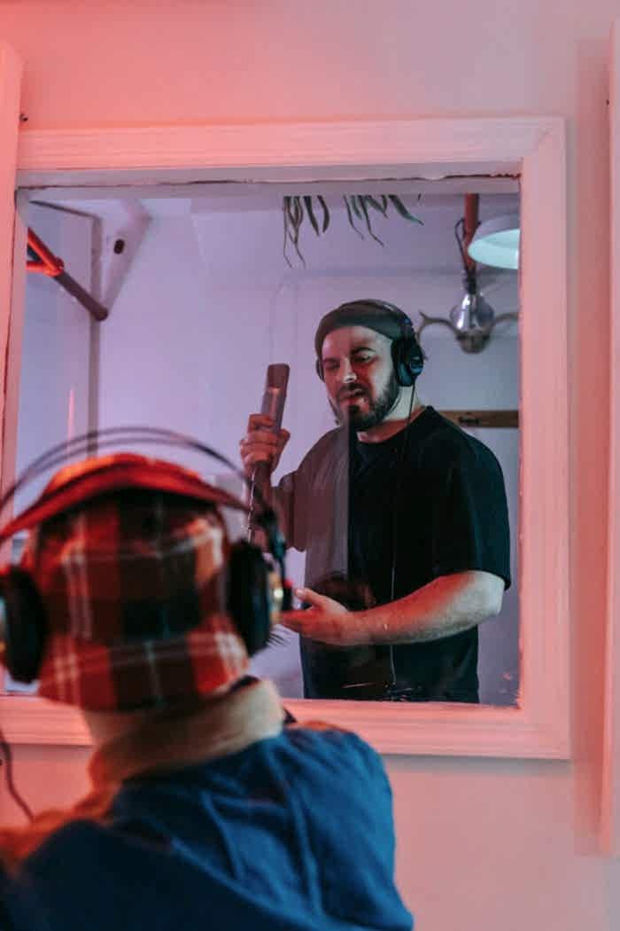 services-02 Bearded man singing into a microphone in a professional music studio.