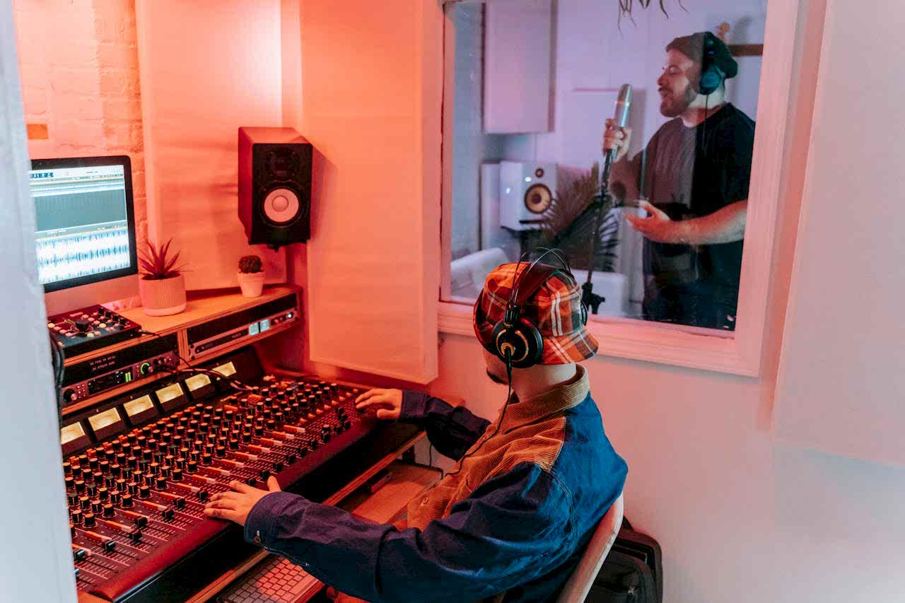 about-01 Two men engaged in a vocal recording session in a modern music studio, highlighting sound equipment.